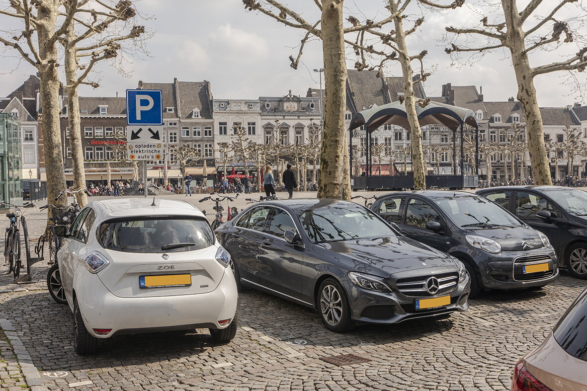Parkeerplaatsen voor elektrische auto's en gewone auto's voor het Vrijthof in Maastricht. Er zijn twee parkeerplaatsen voor elektrische auto's die worden aangeduid met een blauw verkeersbord. Je ziet nog drie parkeerplaatsen voor gewone auto's. Alle parkeerplaatsen zijn bezet.