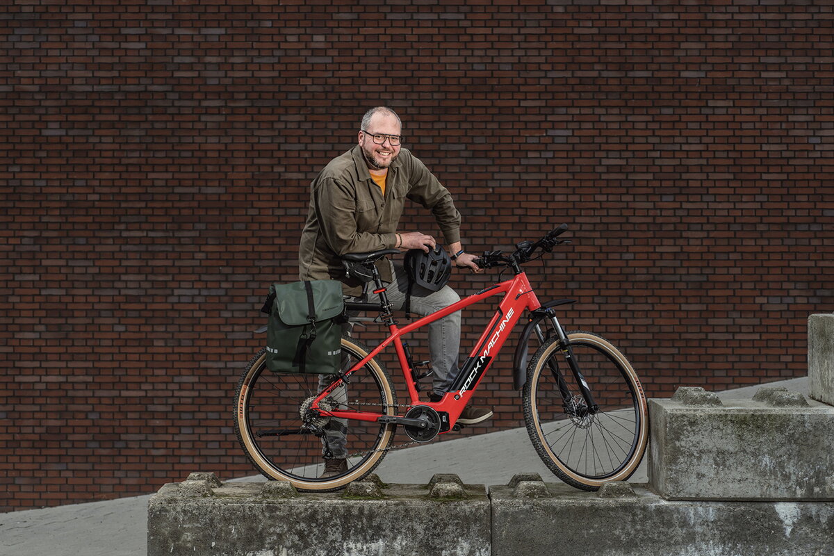   Richard Limpens poseert naast zijn rode elektrische fiets en houdt zijn fietshelm in zijn hand