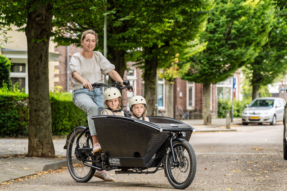 Sofie Leenders met bakfiets in Valkenburg en twee kinderen. Op de achtergrond groene bomen