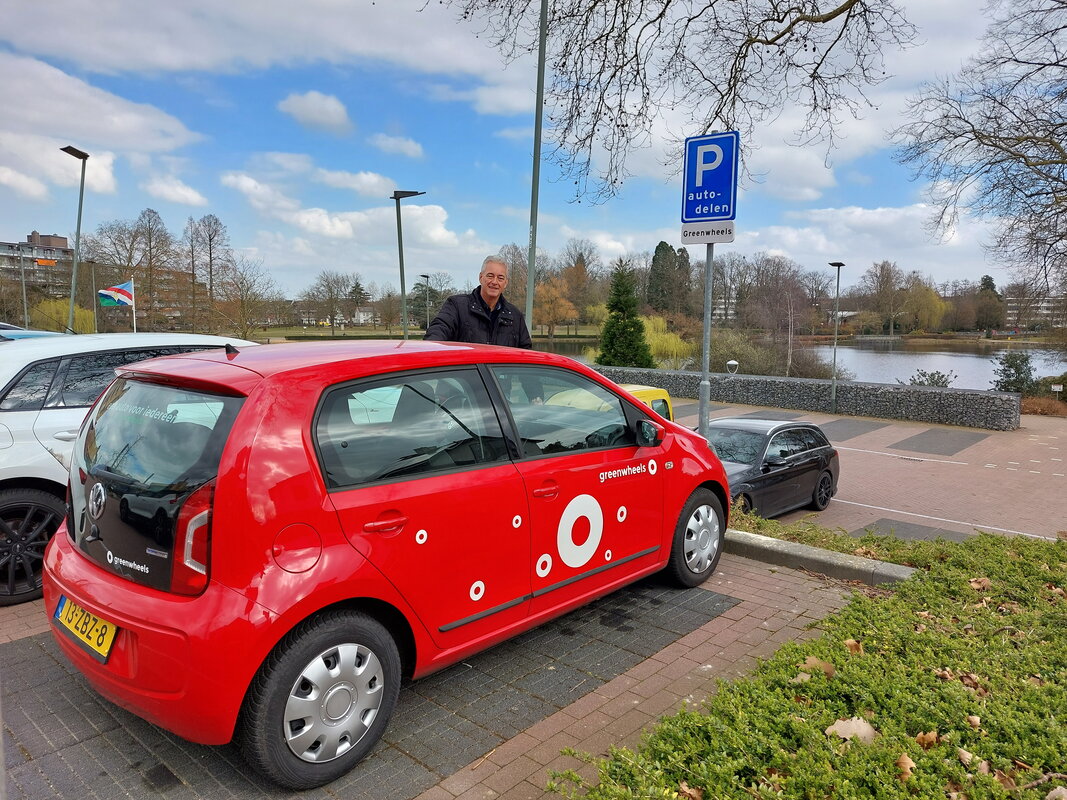 Rode deelauto van Greenwheels op de voorgrond met daarachter wethouder Hugo Janssen van de gemeente Brunssum