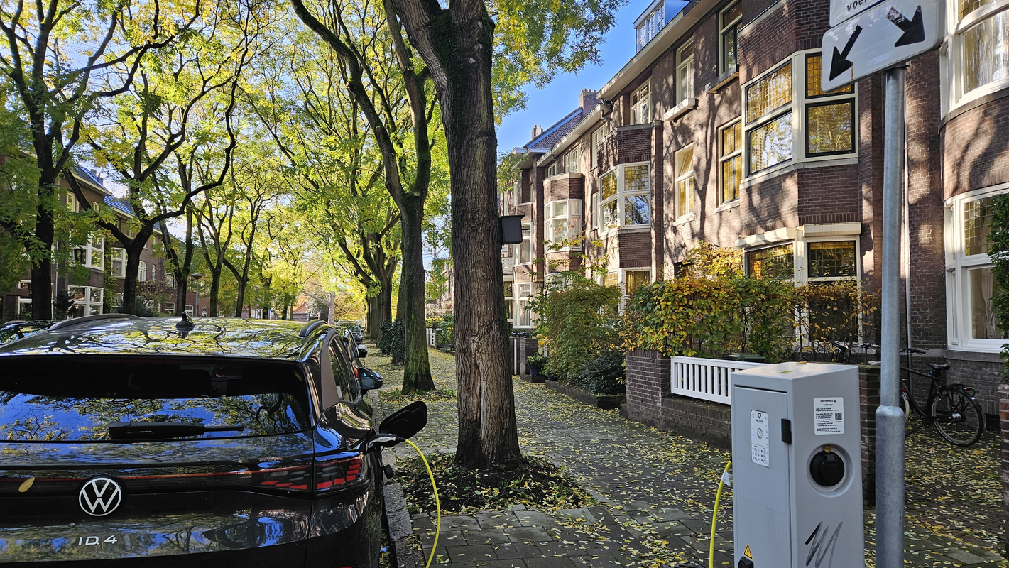 Elektrische auto aan een laadpaal in een woonwijk, straat met bomen 