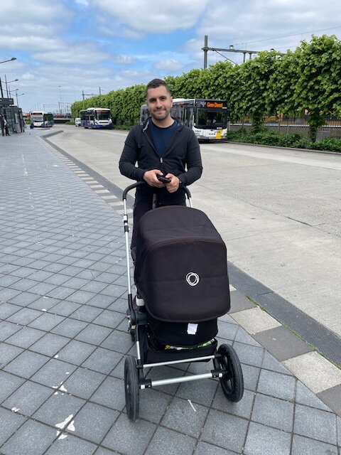 Helmy staat met de kinderwagen bij de bushalte. Op de achtergrond zie je station Maastricht
