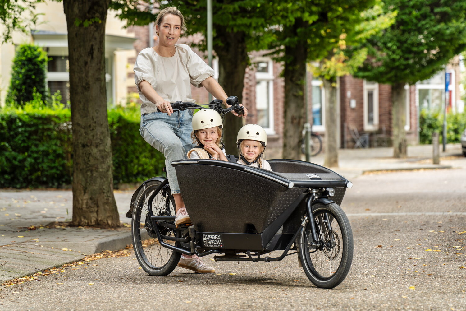 Sofie Leenders op de bakfiets met twee kinderen in Valkenburg. Op de achtergrond staan groene bomen.