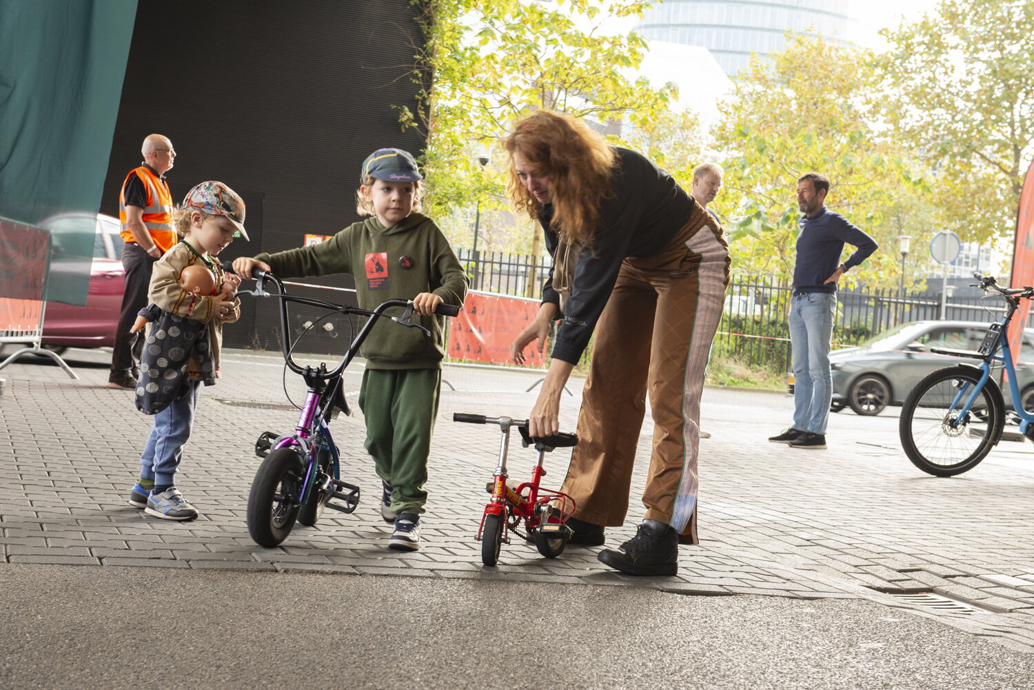 Twee kleine kinderen met twee fiets en een volwassene op het Cargobikefestival. Op de achtergrond staat andere mensen