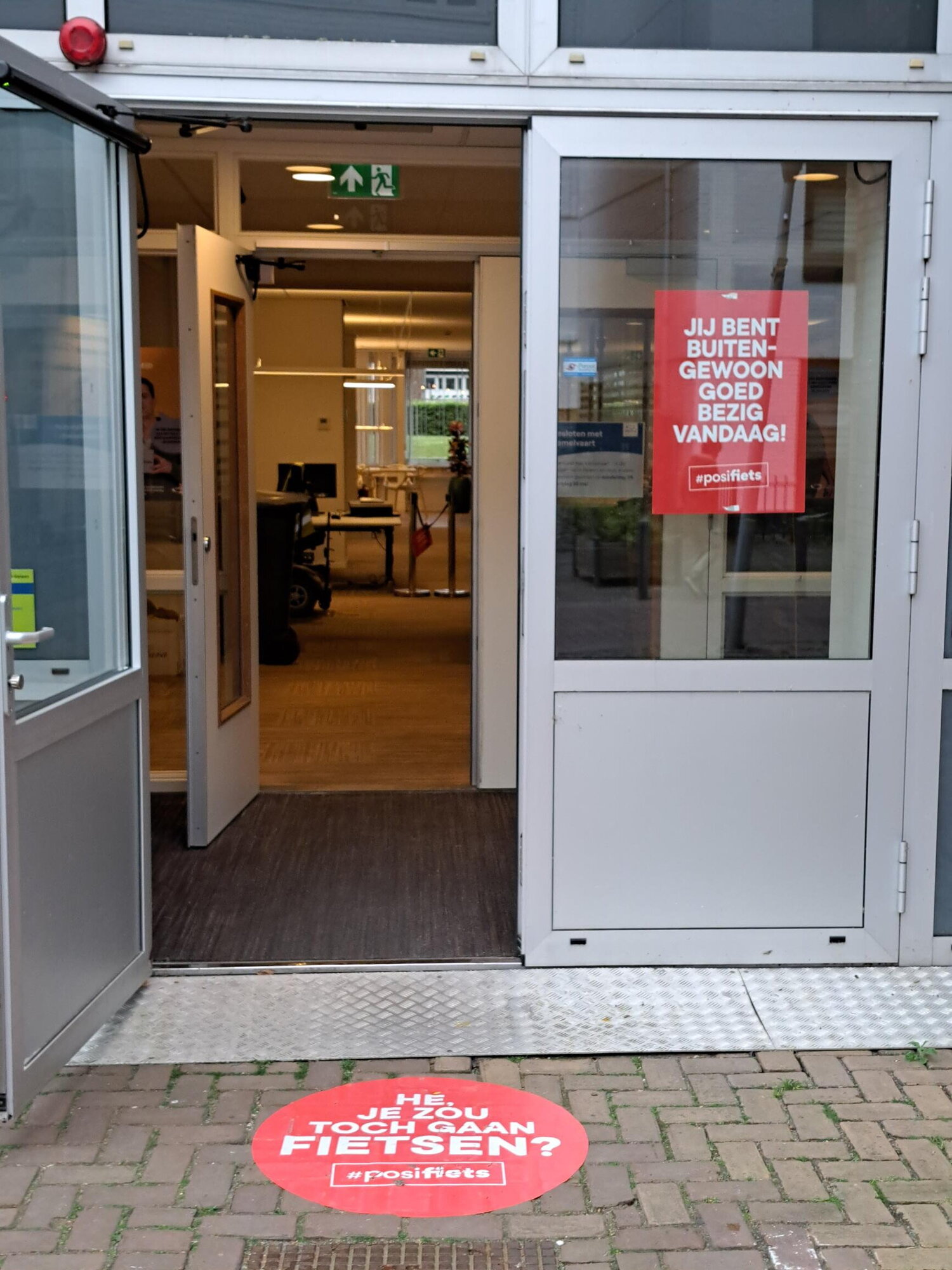 Promotie Fiets naar je Werk Dag bij de gemeente Sittard-Geleen 2025. Je ziet poster met daarop de tekst je bent buitengewoon goed bezig vandaag en een vloersticker met de tekst Hé je zou toch gaan fietsen vandaag?