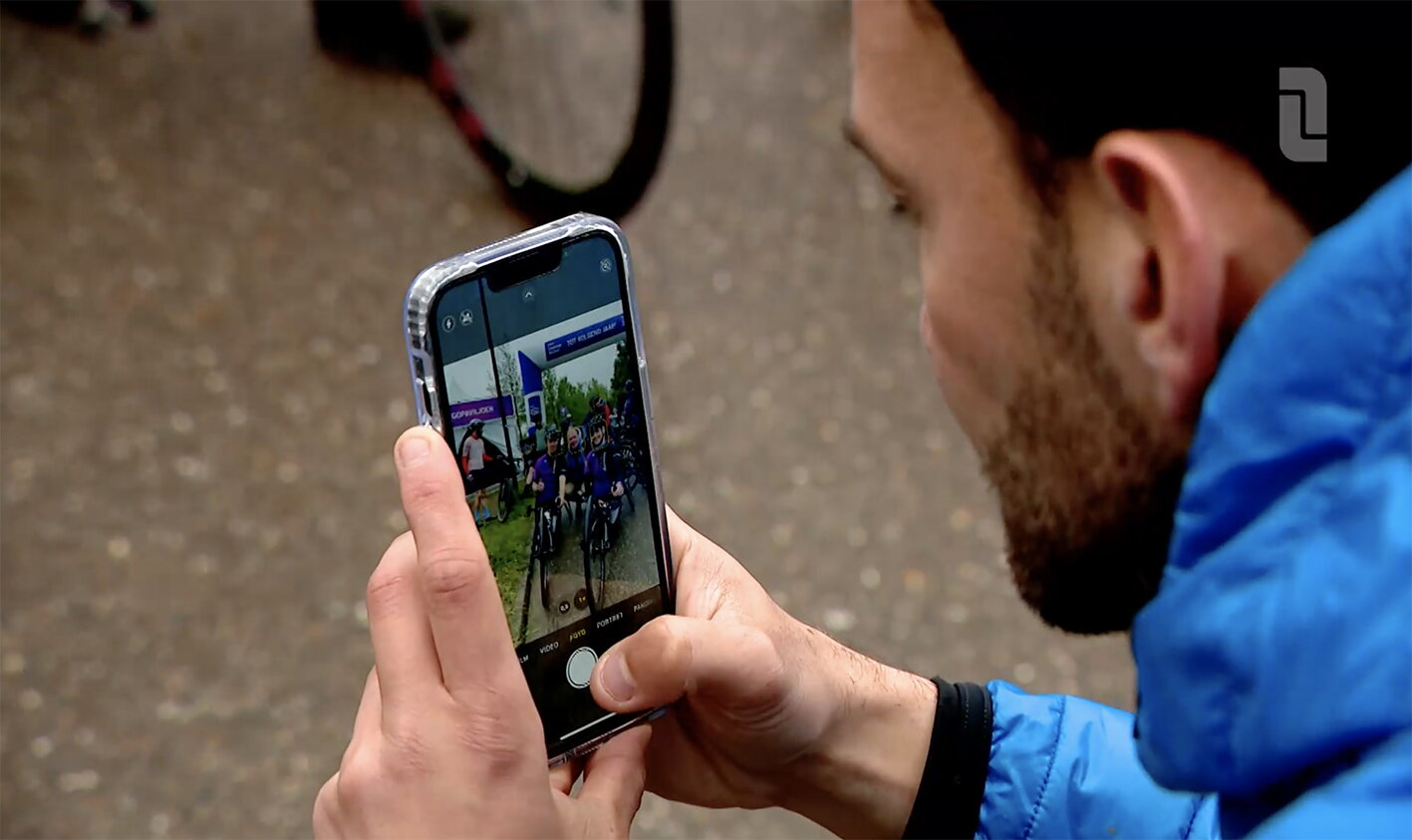 Lars Delnoy in blauwe jas maakt een foto van fietsers tijdens Limburgs Mooiste