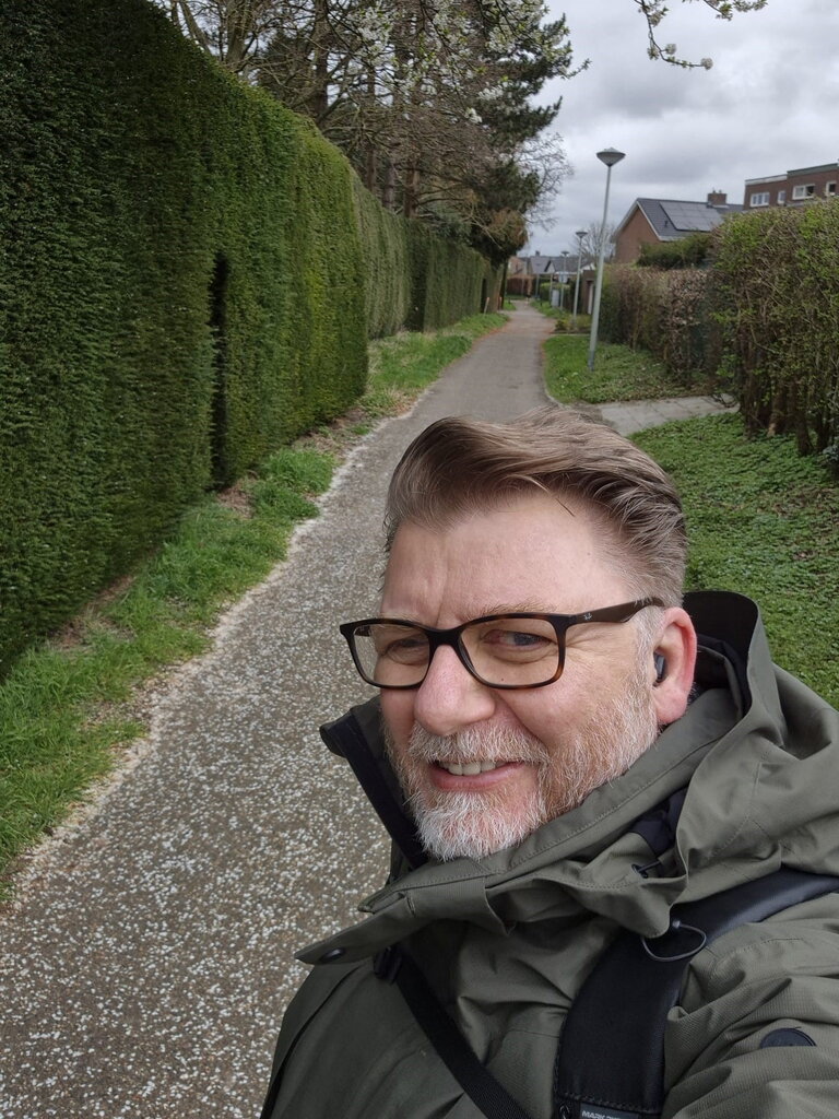 Guido van der Meulen wandelend naar zijn werk bij de gemeente Sittard-Geleen. Hij maakt een selfie terwijl hij loopt op een wandelpad tussen huizen in. 